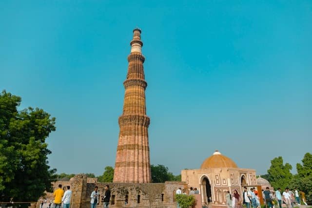 a tall tower with people standing around with Qutub Minar in the background