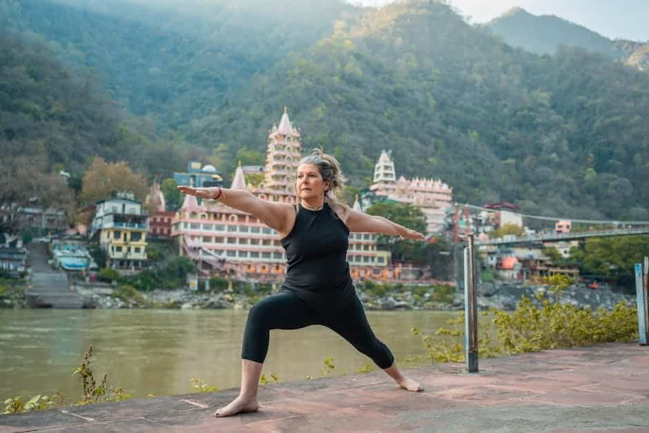 A senior woman doing yoga by the river with Rishikesh's iconic temple in the background.