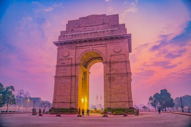 a large stone arch with people walking around with India Gate in the background